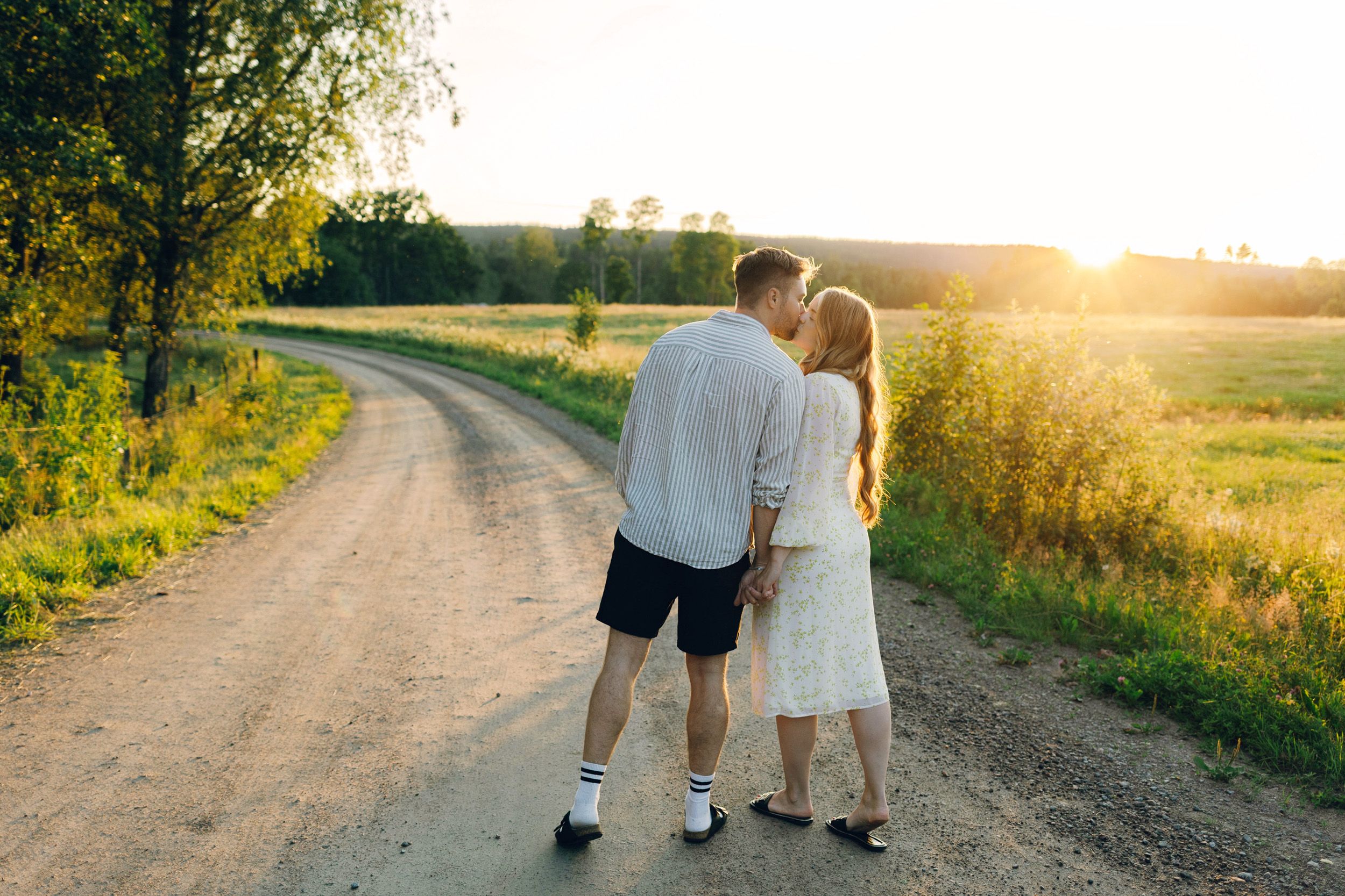 Parfotografering med Martina och Sebastian i Borgvik utanför Karlstad. Gående på grusväg i solnedgång. De kysser varandra.