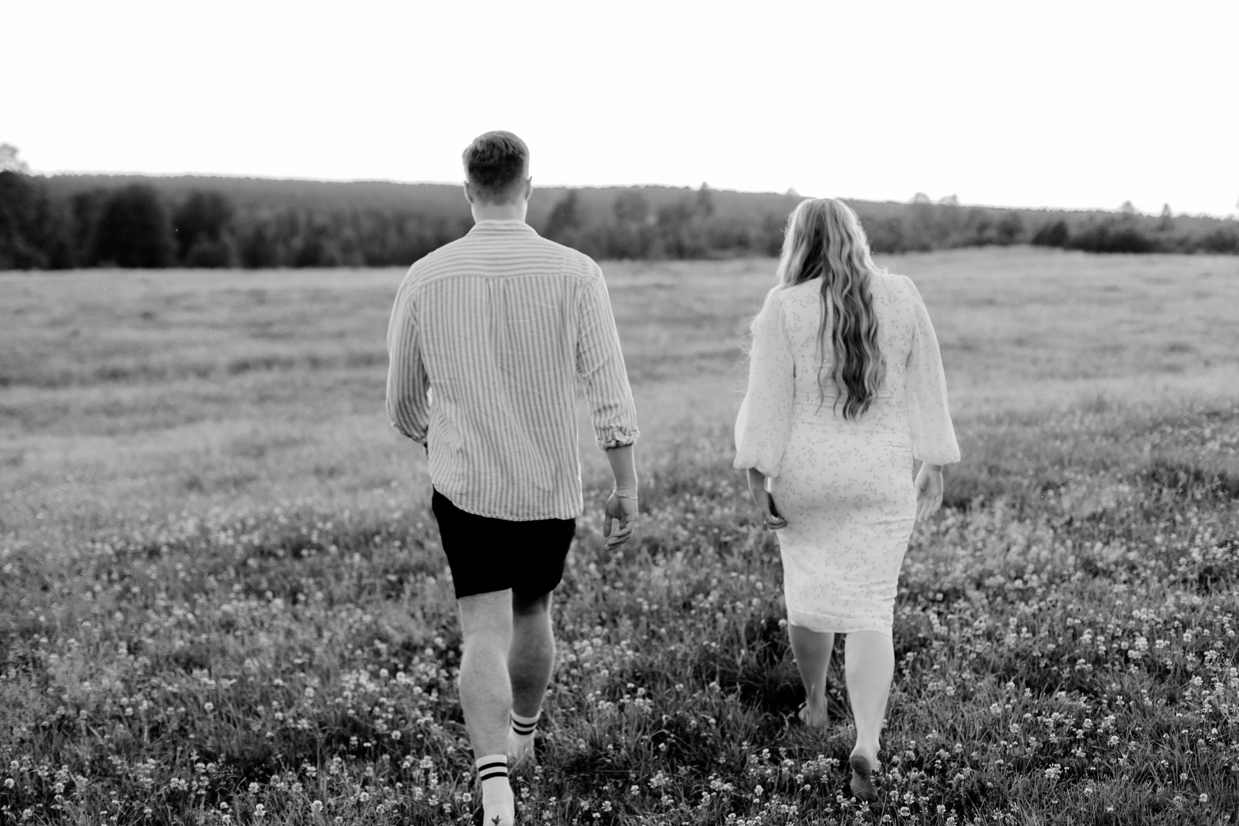 Parfotografering med Martina och Sebastian i Borgvik utanför Karlstad. Går bortåt på en äng tillsammans. Svartvit.