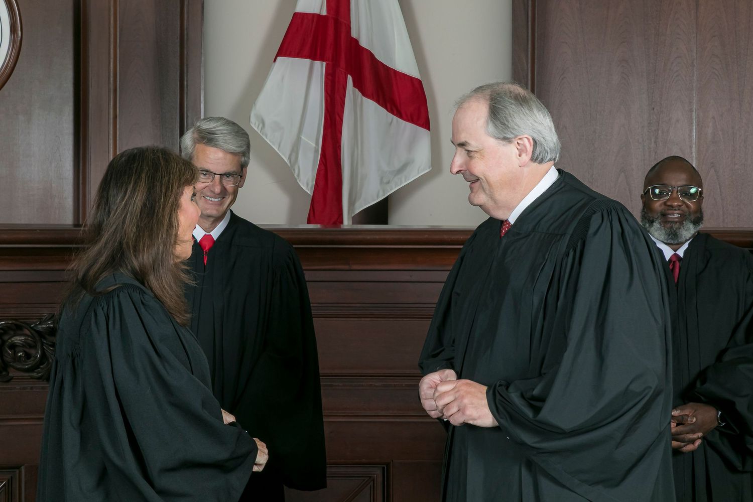 A group of judges in black robes pose together in a formal courthouse setting.