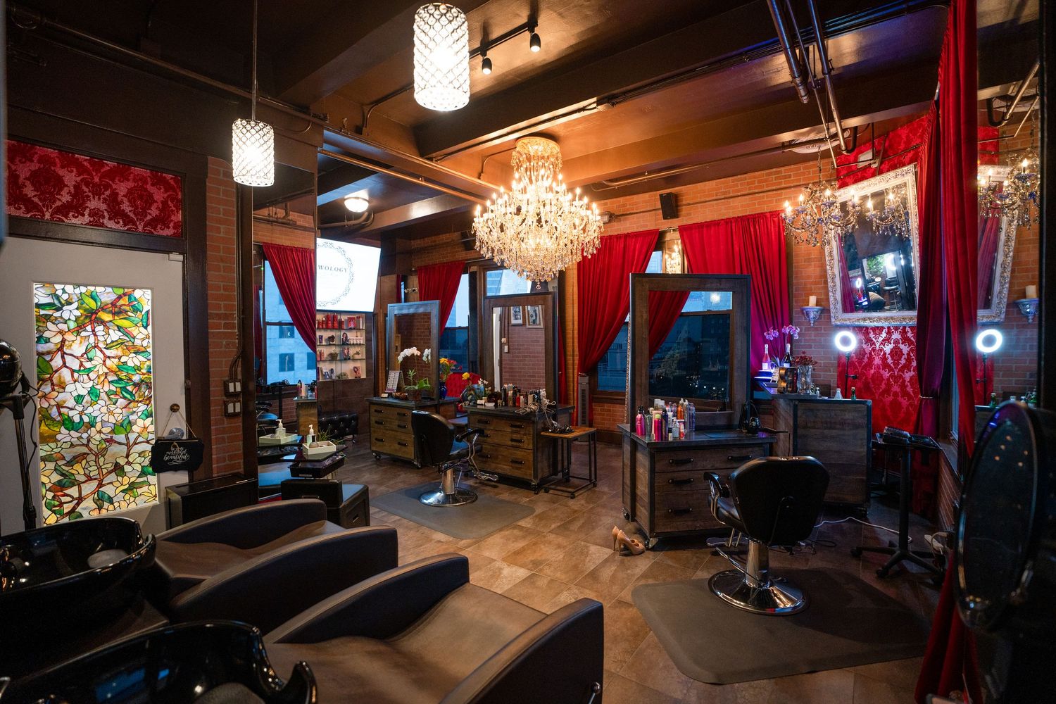 Interior view of a dimly lit bar or lounge with red curtains, chandeliers and exposed brick walls showing multiple angles.
