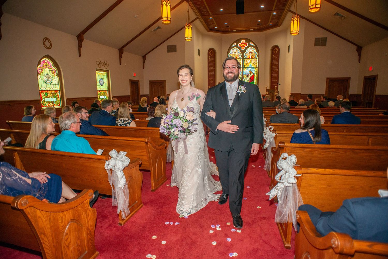A wedding ceremony in progress at a traditional church with wooden pews and stained glass windows.