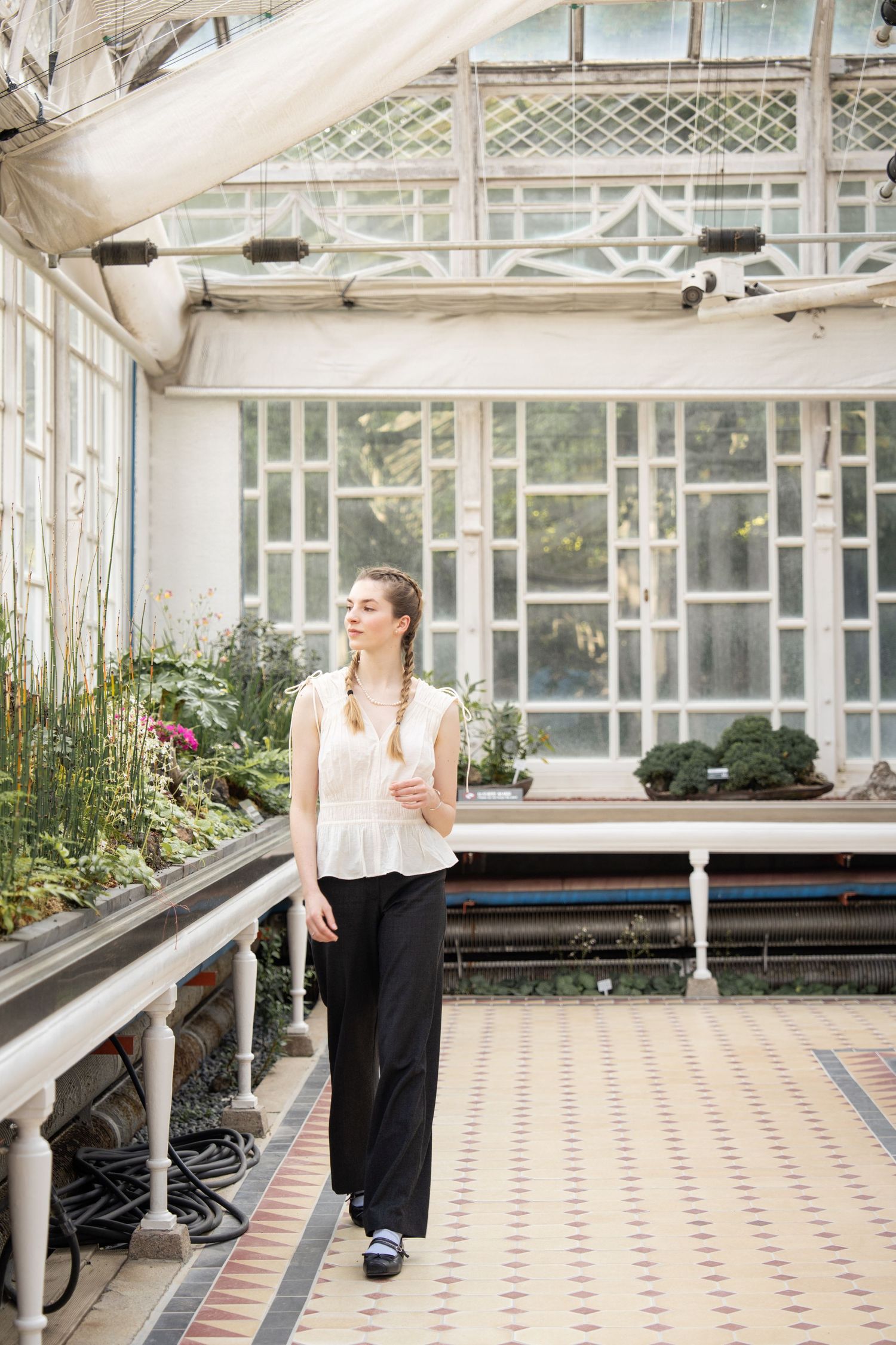 A greenhouse interior with tiled floors and white architectural details features a bright, airy atmosphere.