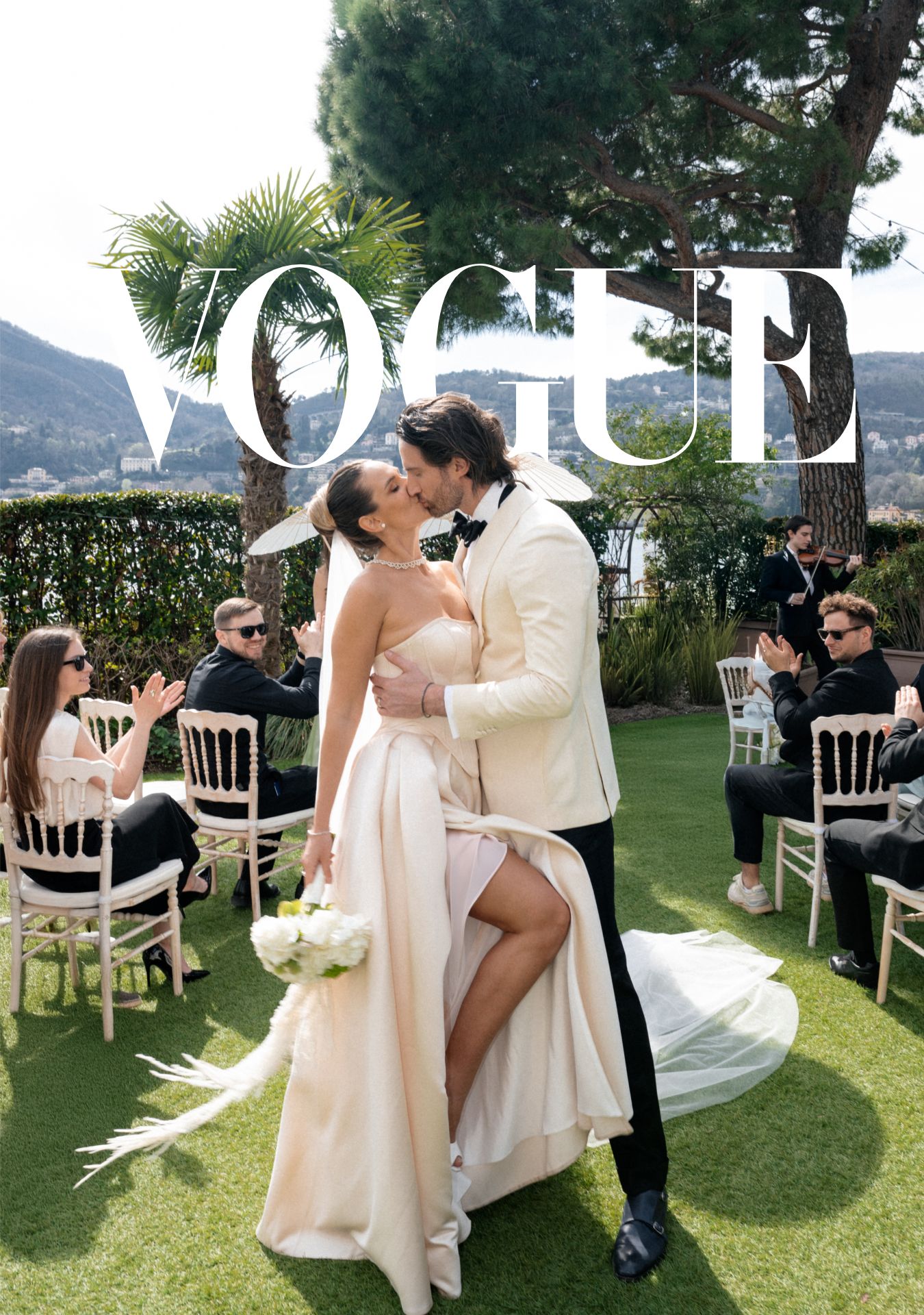 Wedding couple dances together on a scenic outdoor lawn with palm trees and mountains in the background.