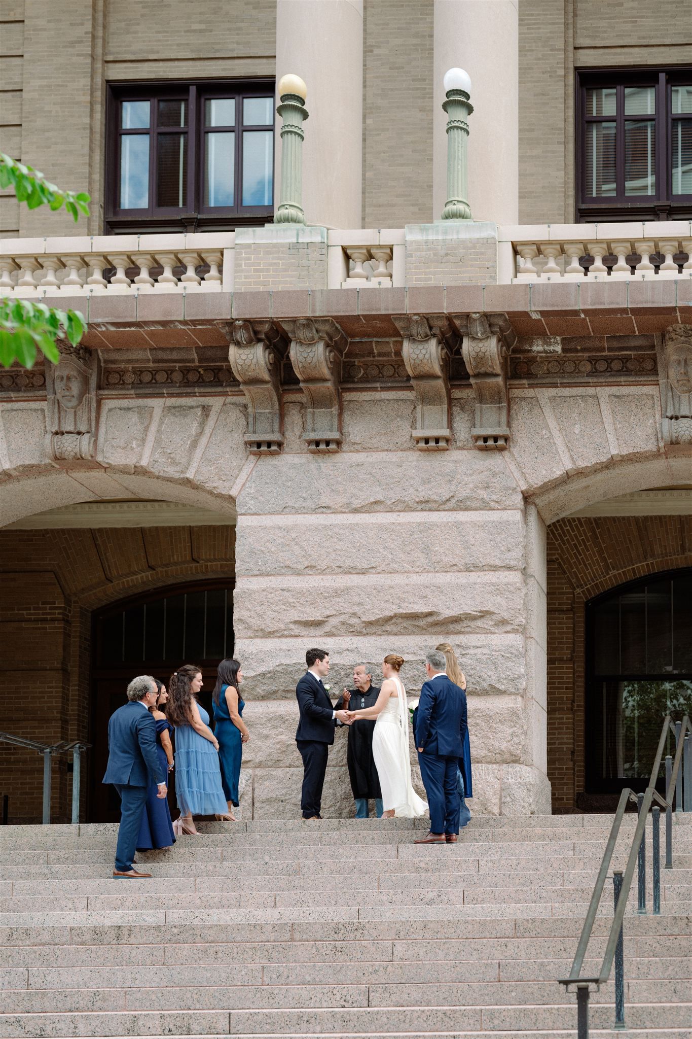 Wedding party stands on stone steps of historic building in progression of candid moments.