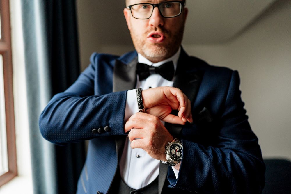 Person in formal attire adjusts their bow tie while sitting near a window in dramatic lighting.