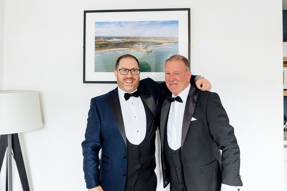 Two people in formal attire pose together while wearing matching black tuxedos and bow ties.