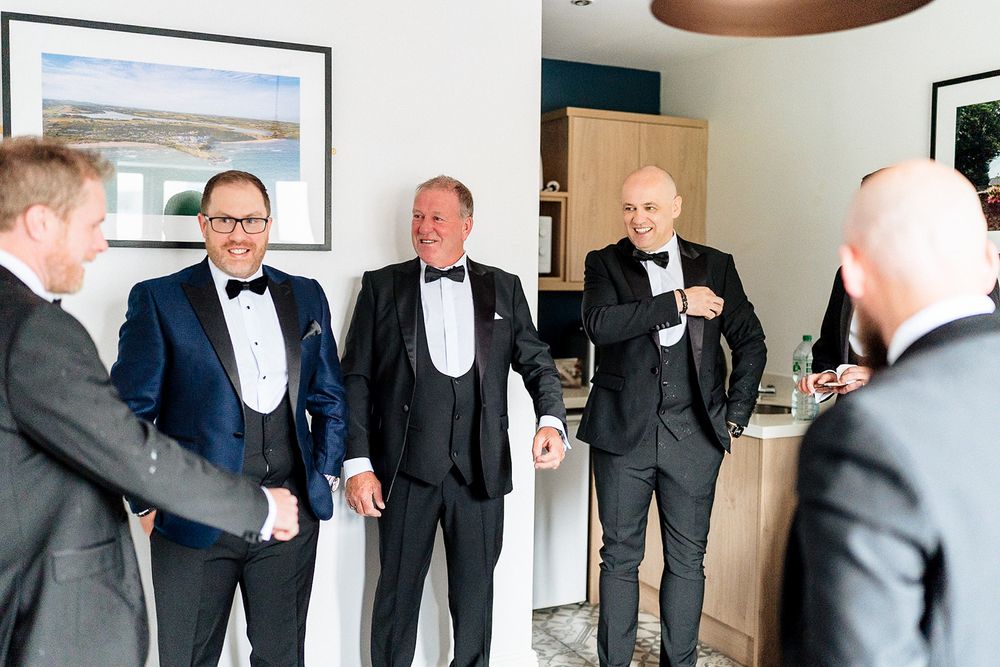 Groomsmen in formal black tuxedos and bow ties getting ready for a wedding celebration.