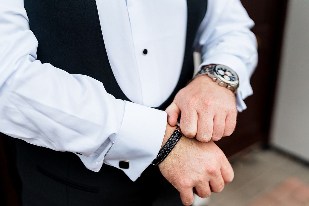 Close-up details of white dress shirt with cufflinks and formal black vest.