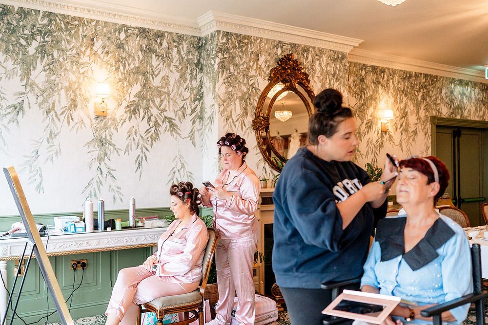 Wedding party members getting ready in a room with floral wallpaper and warm lighting.