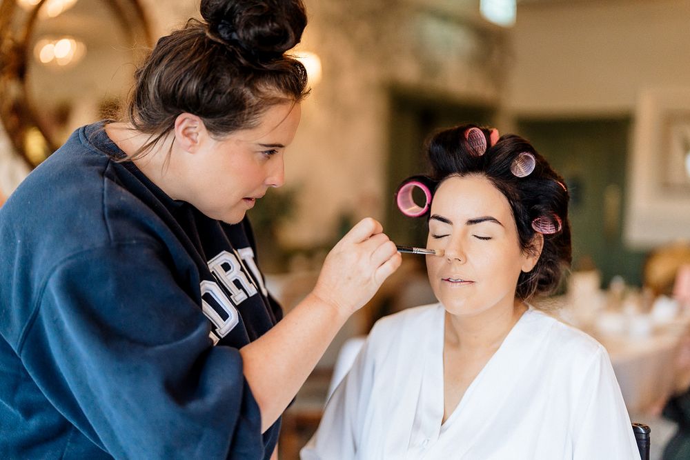 Makeup artist applies cosmetics to someone in a white robe during wedding preparations.