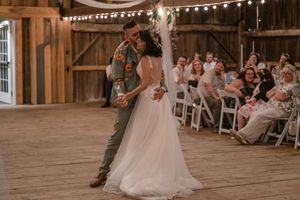 Couple performs their first dance in a rustic barn venue decorated with string lights and wooden beams.