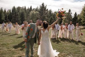 Wedding party poses for photos in an outdoor field with evergreen trees in the background.