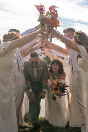 Wedding party in white and sage green attire creating a fun tunnel formation outdoors.
