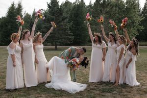 Bridesmaids in light colored dresses pose playfully on the grass for wedding photos.