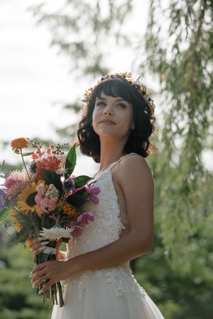 Bride holding vibrant wildflower bouquet with orange and pink blooms against natural backdrop.