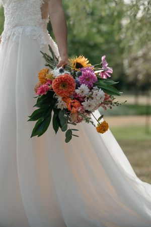A vibrant bridal bouquet with sunflowers and pink flowers against a flowing white wedding dress.