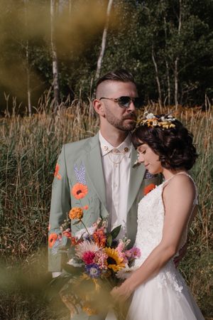Couple in wedding attire posing in tall grass field during golden hour.