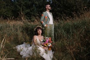 A bride in a flowing white gown poses in tall grass during golden hour.