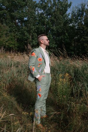 Artistic portrait in tall grass field with orange floral embellishments on clothing.