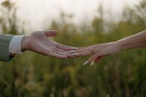Close-up of hands reaching toward each other against a natural outdoor background.