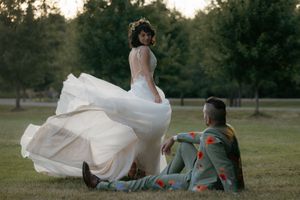 Wedding couple posing playfully in a field at dusk with bride's dress flowing in the wind.