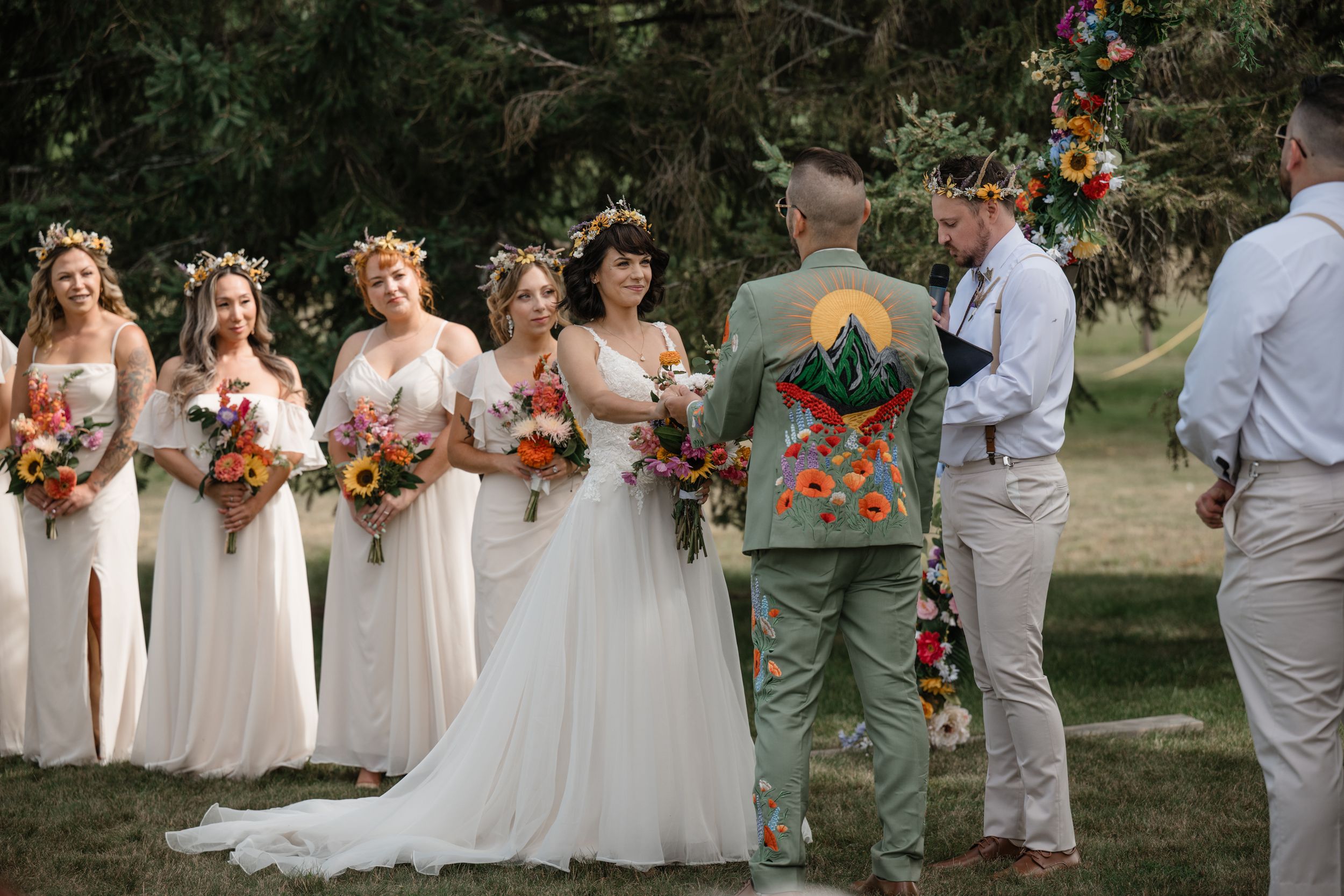 Wedding party stands in line holding colorful bouquets against natural outdoor backdrop.