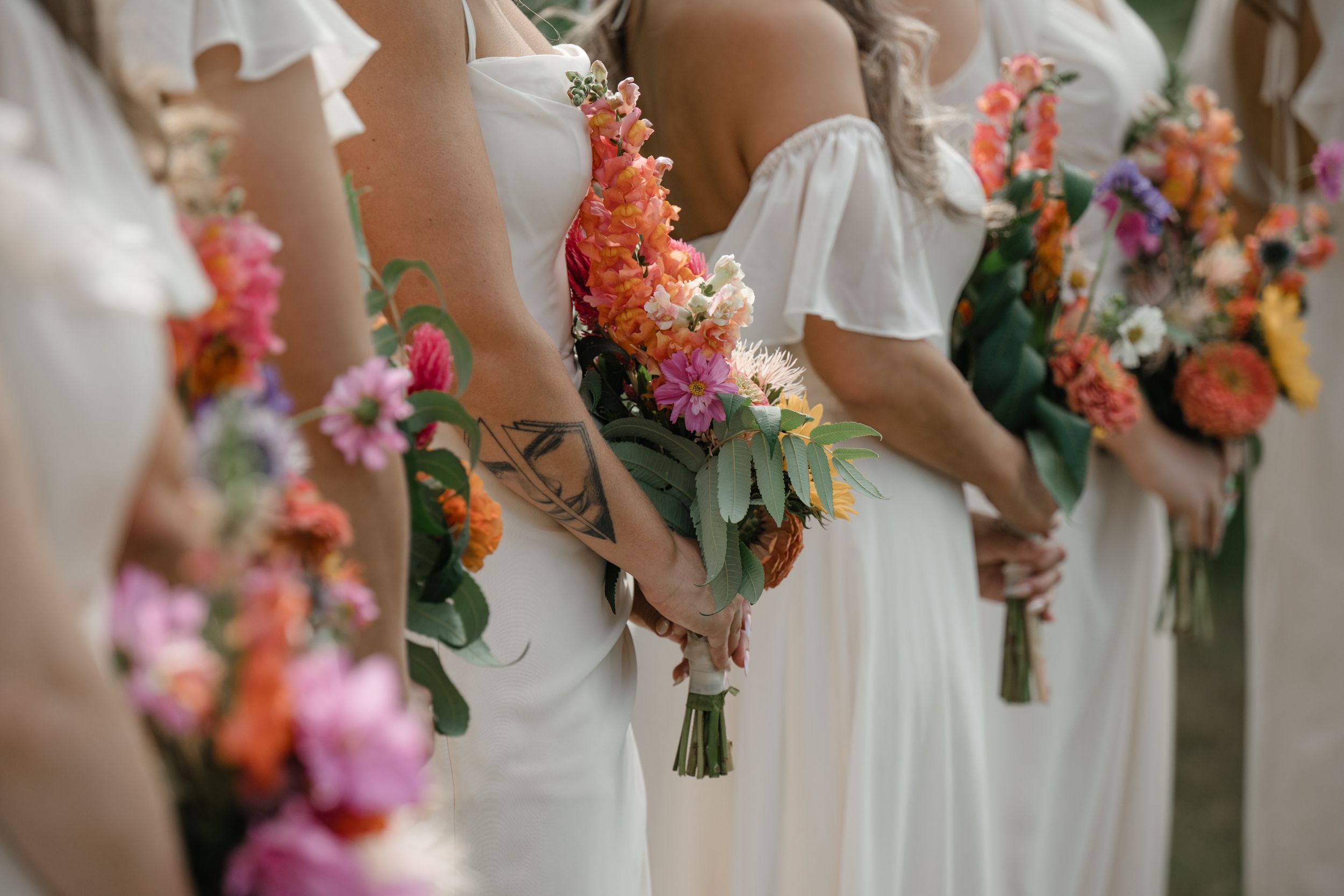 Close-up of vibrant coral and pink wedding bouquets held by people in white dresses.