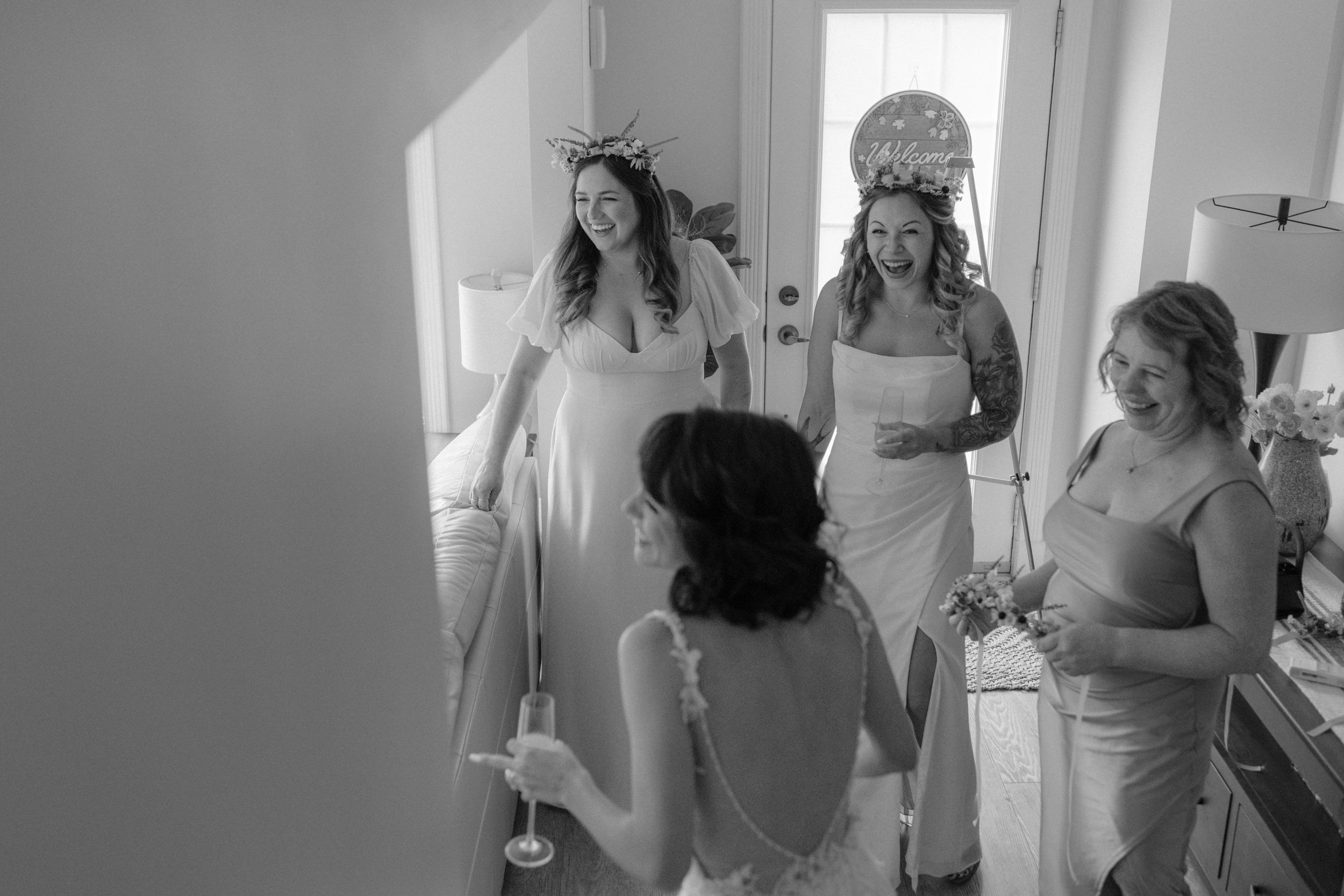 Group getting ready in a bright indoor space wearing white dresses and robes during wedding preparations.