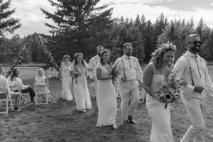 Wedding party in white dresses and suits walking together outdoors in a candid celebratory moment.