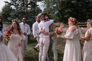 Wedding party in white dresses and suits dancing together in a line outdoors during a celebration.