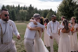 Wedding party celebrates outdoors with dancing and laughter in a scenic field setting.