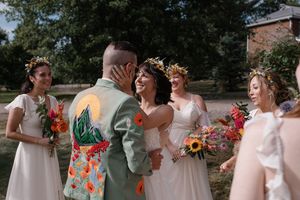 Wedding party wearing white dresses and sage green suits posing with vibrant autumn bouquets.