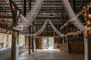 Rustic wooden barn interior with exposed beams and string lights creating an atmospheric wedding venue space.