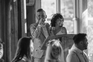 Wedding party members dance and celebrate joyfully inside a rustic venue with natural lighting.