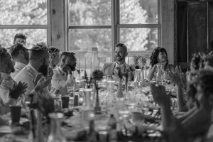 Wedding reception guests raise their glasses in celebration at a sunlit venue with large windows.