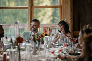 A panoramic view of guests seated at dining tables in a rustic restaurant with large windows overlooking nature.
