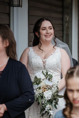 A bride in a white lace wedding dress holds a delicate bouquet of white flowers and greenery.