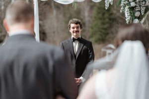 A wedding ceremony scene showing a groom in a black tuxedo standing at the altar.