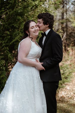 A tender moment between newlyweds in formal attire embracing outdoors among greenery.