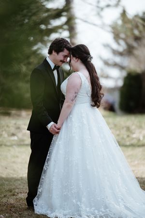 A romantic wedding moment captured outdoors showing a couple in formal attire with a flowing white lace gown.