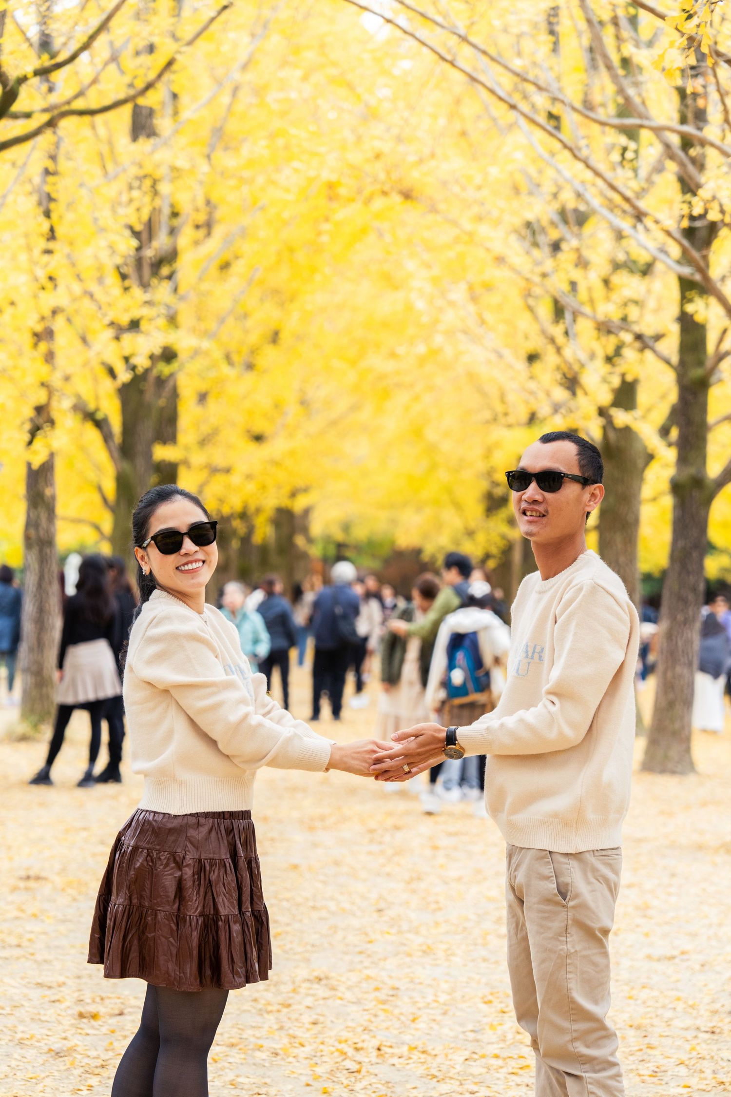 A couple dances together on a path lined with bright yellow autumn trees while others walk in the background.