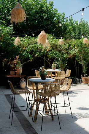 Outdoor patio dining area with rattan chairs and hanging grass decorations under string lights.