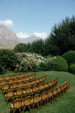 Wooden cross-back chairs arranged in rows on a lush green lawn with mountains and trees creating a scenic outdoor venue setting.