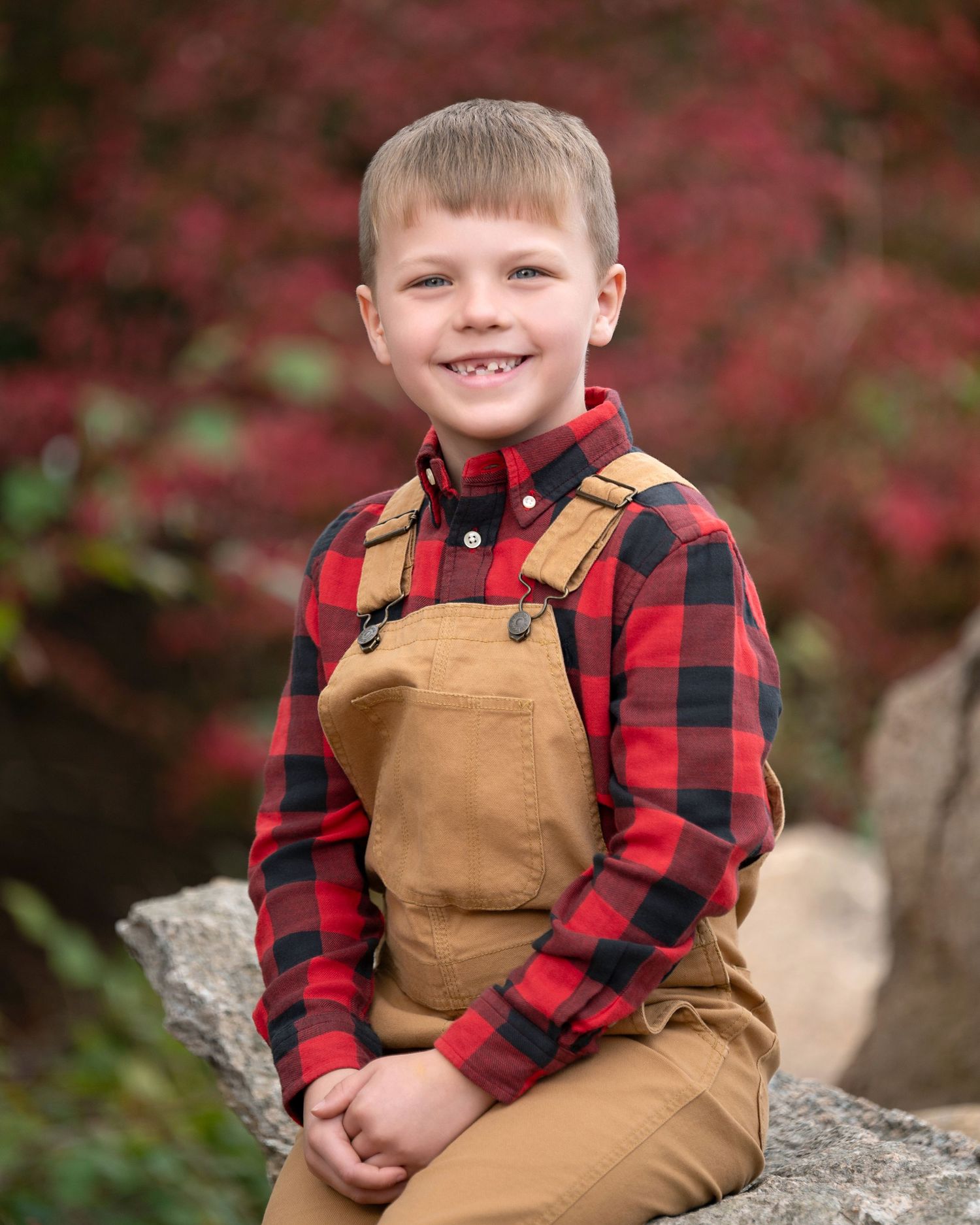 Child in light blue button-down shirt sitting on furry surface with green foliage background.