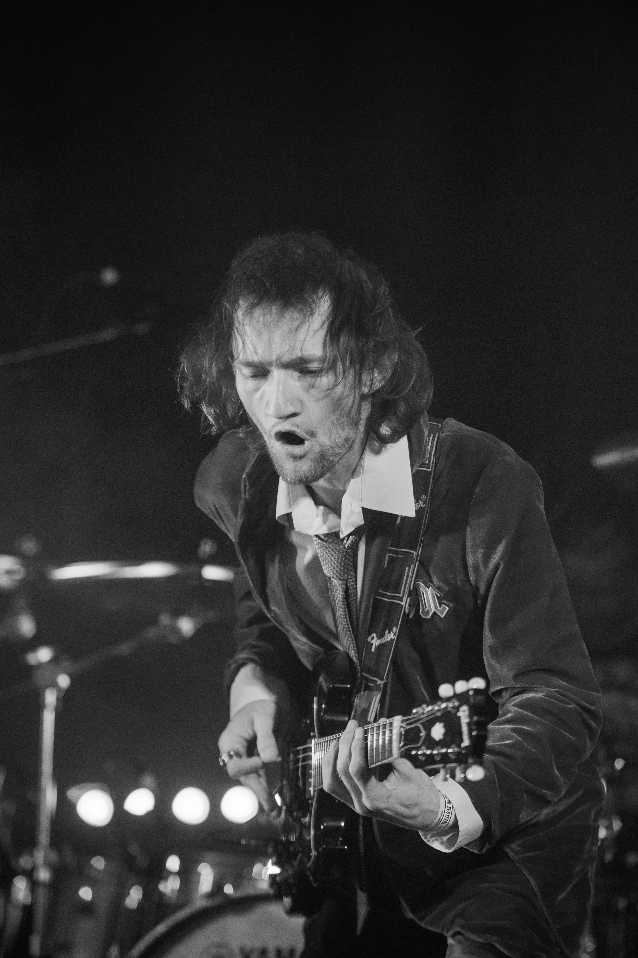 Black and white concert photo of a rock guitarist performing energetically on stage with an electric guitar.