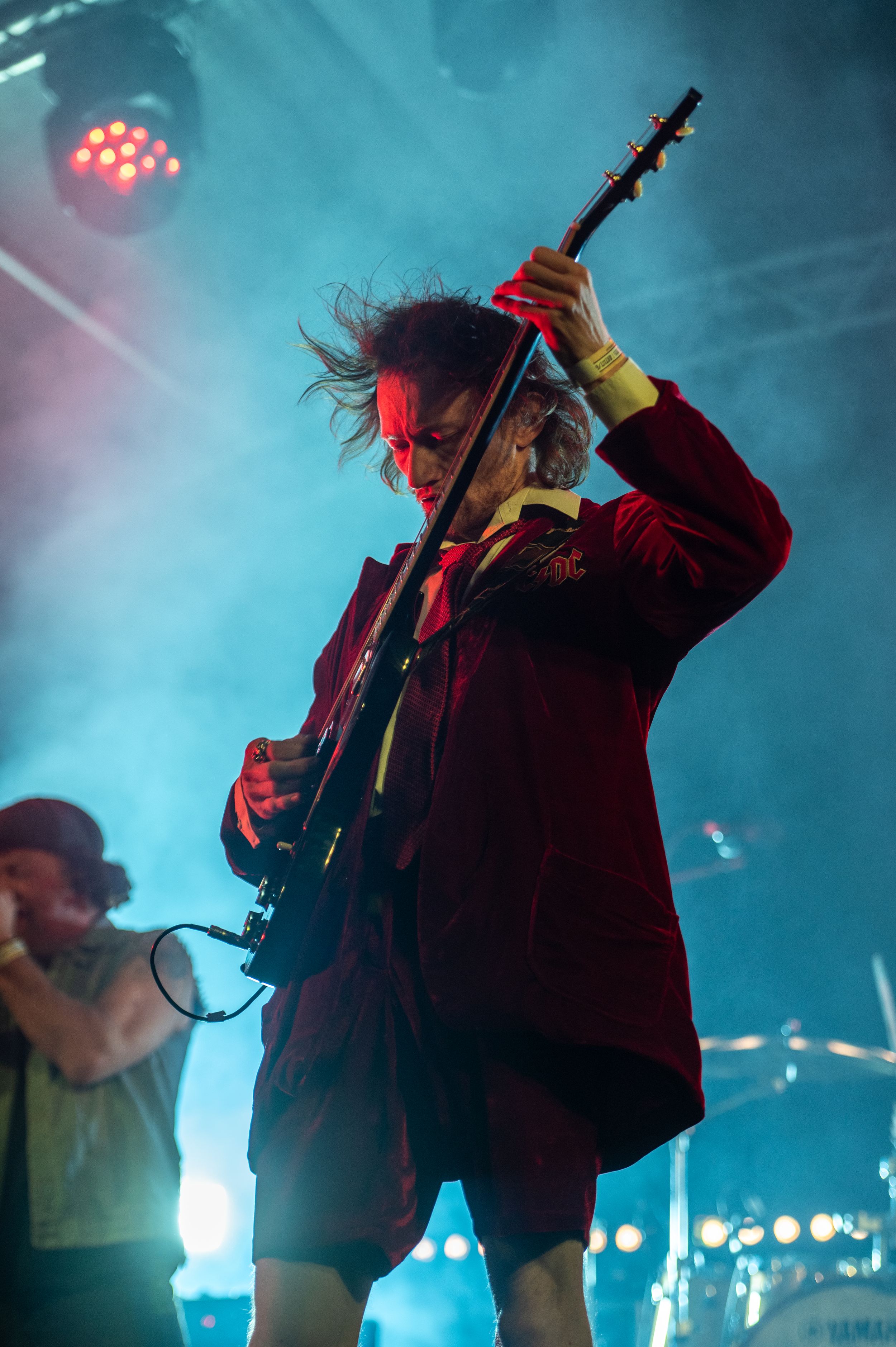 A performer silhouetted on stage plays guitar amidst blue and red atmospheric lighting during a concert performance.