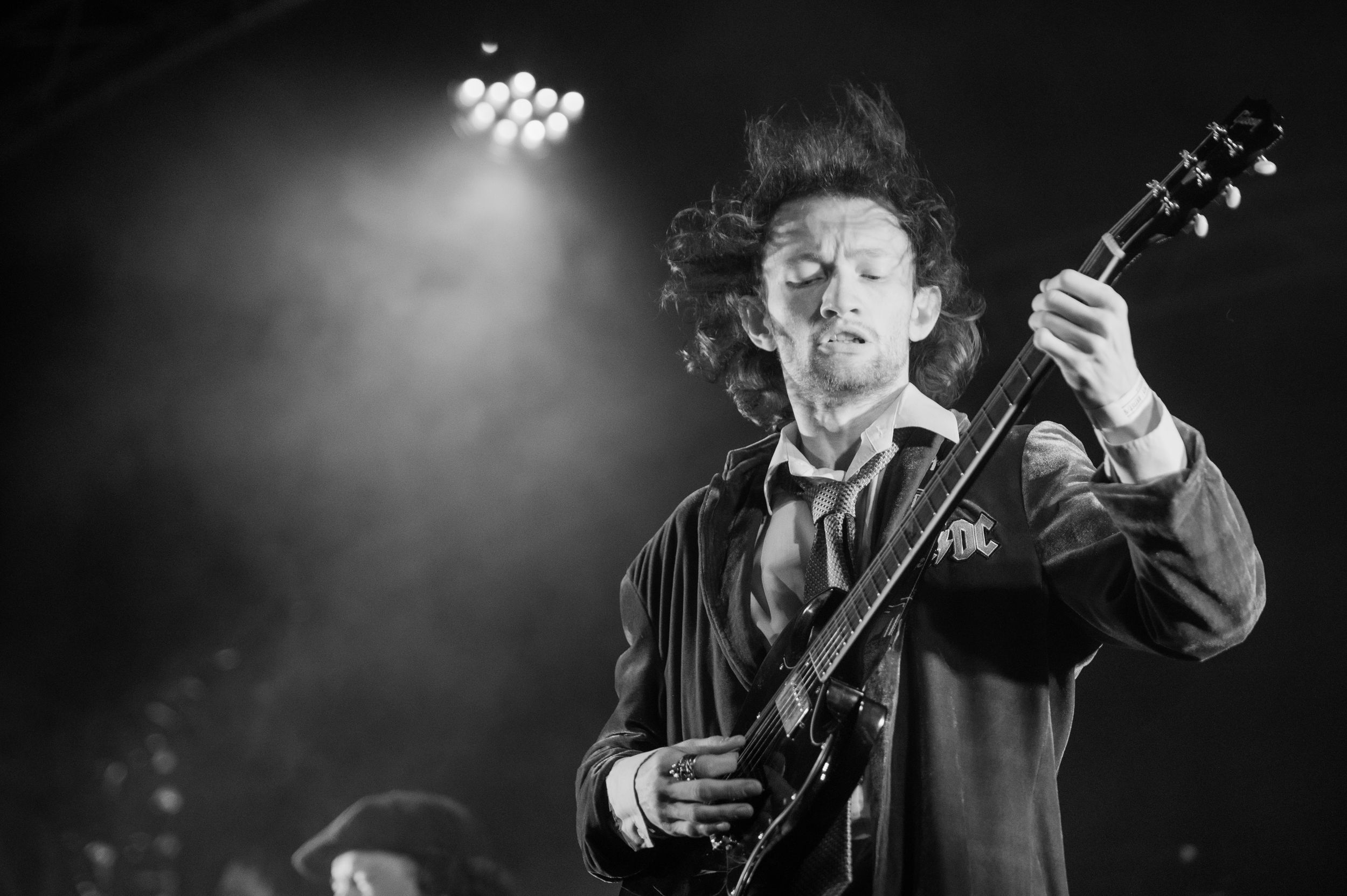 A black and white performance photo showing a guitarist playing on stage under dramatic lighting.