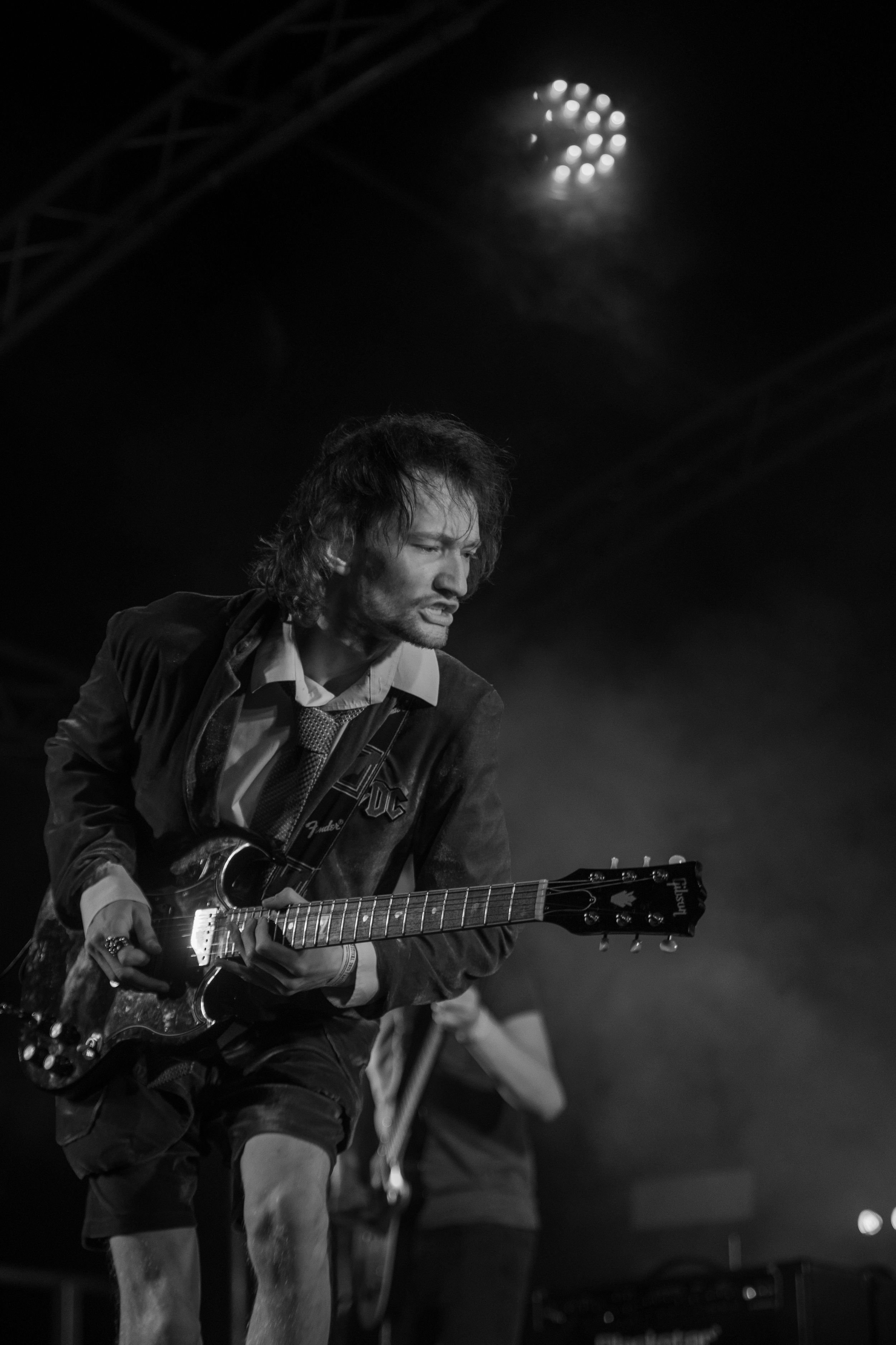 Dramatic black and white stage photo of a guitarist performing under spotlight during a rock concert.
