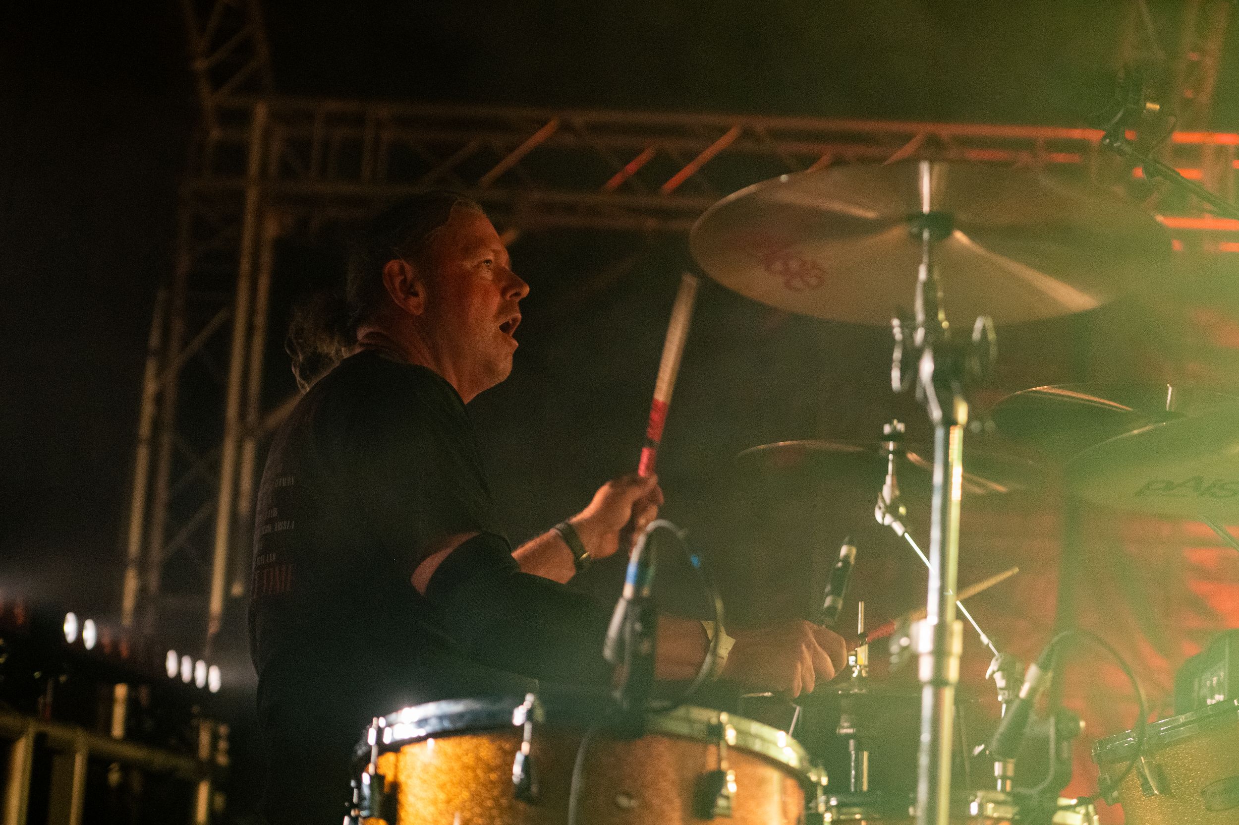 Drummer performing on stage with dramatic lighting and smoke effects during a live concert performance.