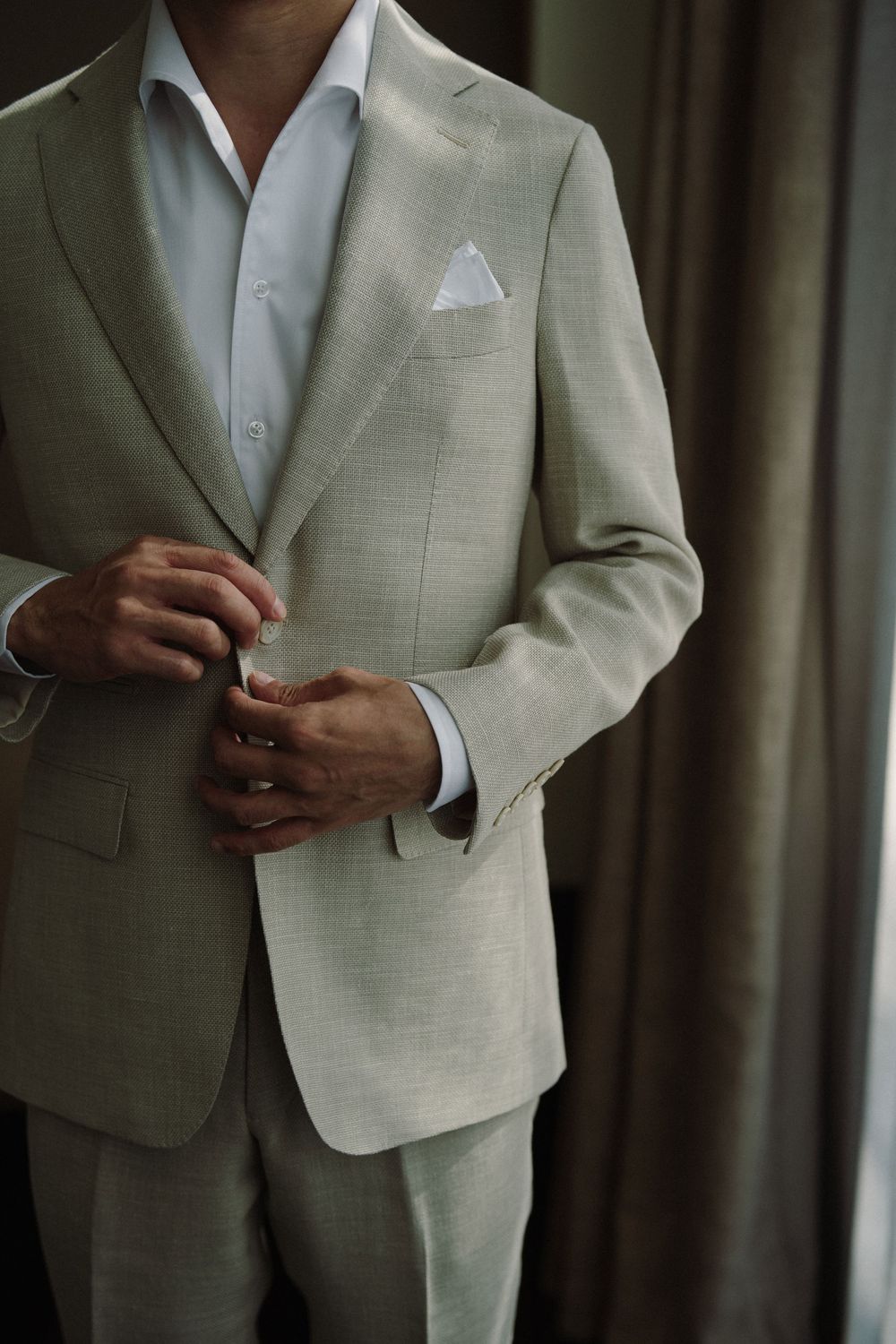 A groom adjusts his light beige suit jacket while getting ready for a wedding ceremony.